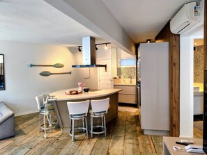 A compact kitchen with a central island, bar stools, a refrigerator, and a microwave.