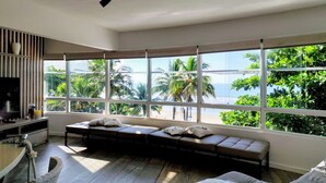 A modern living room with a large window, a sofa, and a TV. - Condomínio Praias do Guarujá (Guarujá)