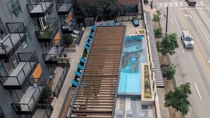 Un edificio de varios pisos con una terraza en la azotea, mobiliario exterior y una piscina.