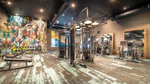 A gym with various exercise equipment, a graffiti wall, and brick walls.
