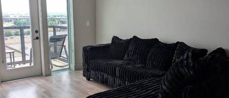 A spacious living room with a dark-colored sectional sofa, a ceiling fan, and a sliding glass door leading to an outdoor patio.