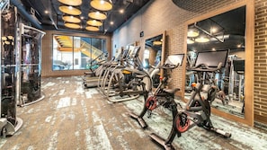 A gym with exercise equipment, a brick wall, and a large window with a view of the street.