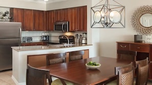 A kitchen with wooden cabinets, a stainless steel refrigerator, a built-in oven, and a dining area with a wooden table and chairs. - Key West 2BR Retreat – Ocean Views & Island Adventure (Key West)
