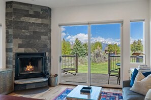 Una sala de estar con chimenea, un sofá, una mesa de centro y vistas a una terraza con mobiliario exterior.