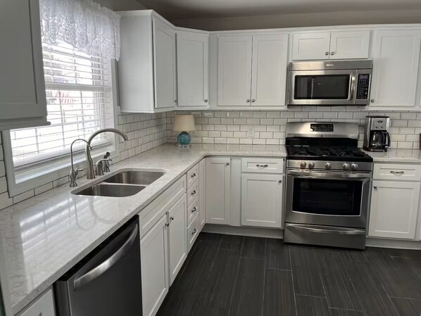A modern kitchen with white cabinets, stainless steel appliances, a dishwasher, and a window with blinds.