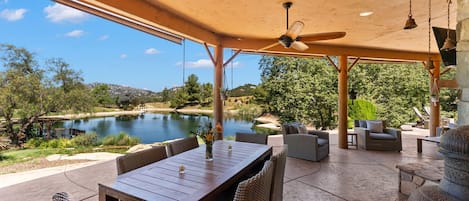 An outdoor patio with a table and chairs, a ceiling fan, and a view of a lake.