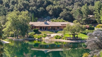A large house with a patio overlooking a lake, surrounded by dense forest.
