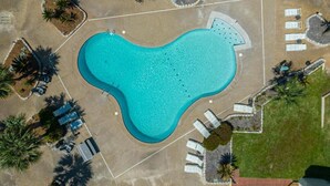 Vista aérea de una piscina rodeada de tumbonas y palmeras.