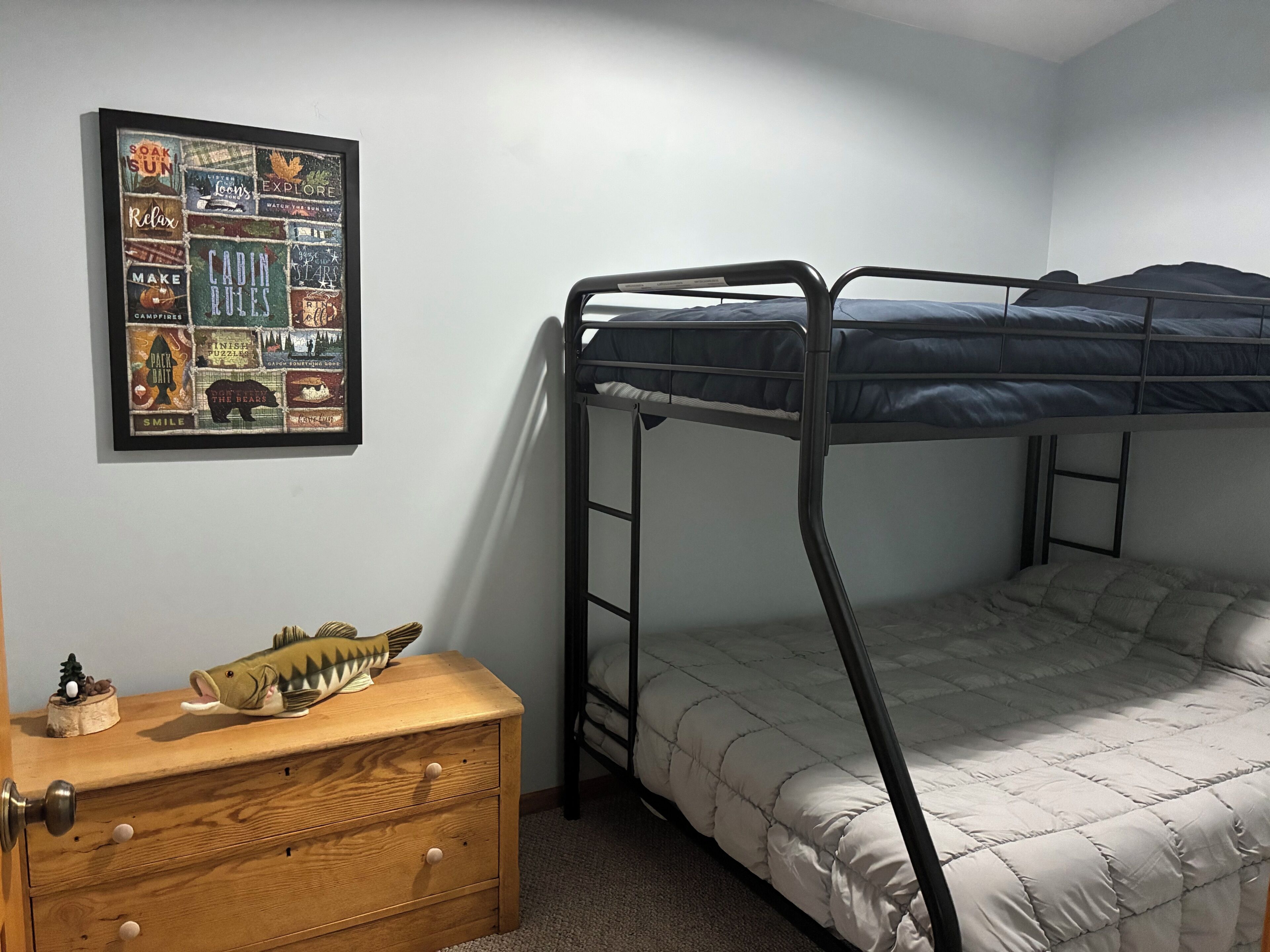 A bunk bed room with a framed poster on the wall, a wooden dresser, and a small fish figurine.