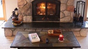 A stone fireplace with a mantel, a glass coffee table in front, and a lit candle.