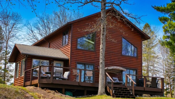 A log cabin with a deck, large windows, and a staircase leading to the upper level.