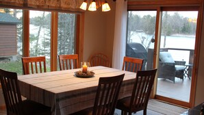 A dining area with a table, chairs, a candle, and a view of a deck and outdoor furniture.