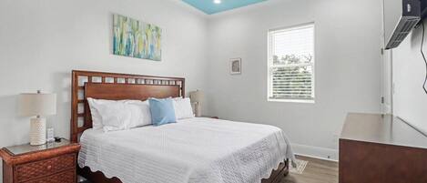 A bedroom with a wooden bed, a nightstand, a lamp, a painting, a window, and a ceiling fan.