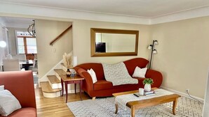 A living room with a red sofa, a coffee table, a patterned rug, a staircase, and a large mirror on the wall. - Stylish 2BR + Office | Near Cleveland Clinic+Shops (South Euclid)