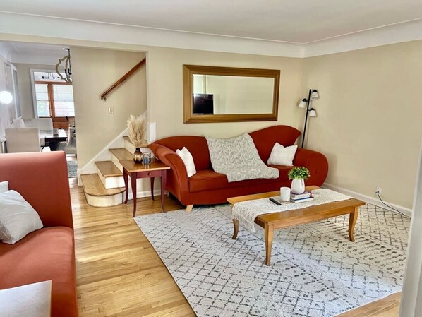 Un salon avec un canapé rouge, une table basse, un tapis à motifs, un escalier et un grand miroir au mur.