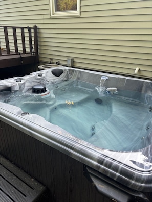 A hot tub outdoors with a wooden deck and a house in the background.