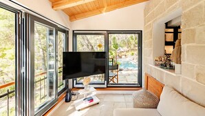 Ein modernes Wohnzimmer mit großem Fernseher, Kamin aus Naturstein und Blick auf einen Pool im Freien.