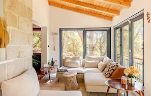 Una sala de estar acogedora con pared de piedra, techo de madera, un juego de sofá, una mesa de centro y un ventanal con vistas a árboles.