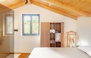 Un dormitorio con techo de madera, una ventana, un armario, una cama y una mesita de noche.