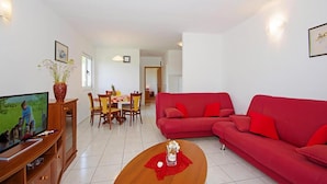 A living room with a red sofa, a wooden coffee table, a TV, and a dining area with a table and chairs. - Gorgeous apartment in Necujam with WiFi (Necujam)