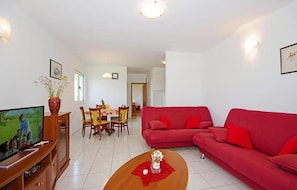A living room with a red sofa, a wooden coffee table, a TV, and a dining area with a table and chairs. - Gorgeous apartment in Necujam with WiFi (Necujam)