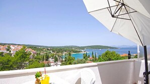 A balcony with a white umbrella, a table with drinks, and a view of a coastal town and sea. - Beautiful apartment in Necujam with WiFi (Necujam)