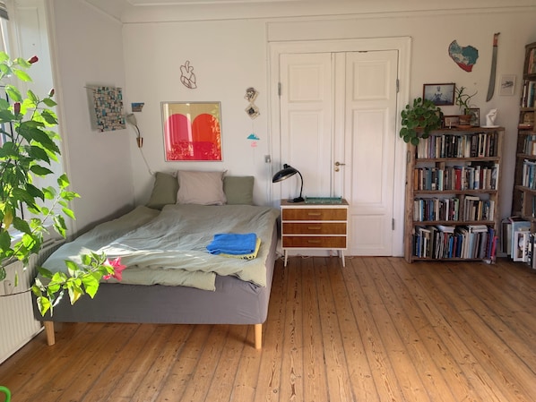 A bedroom with a bed, bedside table, lamp, dresser, and a bookshelf.