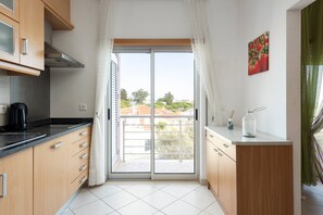 Eine Küche mit einer Schiebetür zum Balkon, Holzschränke, einer schwarzen Arbeitsplatte und einer kleinen Vase mit einem Glasgefäß.