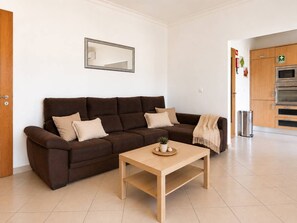Ein modernes Wohnzimmer mit einem braunen Sofa, einem Holztisch und einer Küchenzeile mit Edelstahlgeräten.