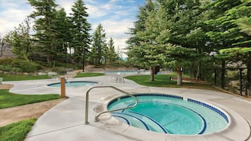 A swimming pool with a tiled edge, surrounded by a concrete deck, with chairs and a small table nearby.