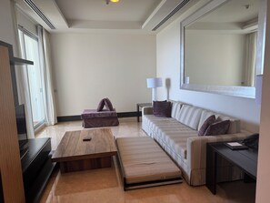 Ein modernes Hotelzimmer mit Sofa, kleinem Tisch, Couchtisch, Fernseher und einem großen Spiegel.
