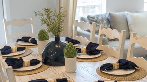 Mesa posta com pratos, guardanapos e um vaso com folhagem.