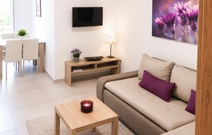 Ein modernes Wohnzimmer mit einer Couch, einem Couchtisch, einem Fernseher und einem Essbereich mit Stühlen und einem Tisch.