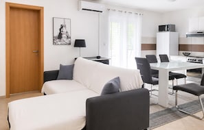 A modern living room with a sofa, a dining table with chairs, a kitchen area with a stove, and a door. - Stunning apartment in Tribanj Sibuljina with WiFi (Tribanj Sibuljina)
