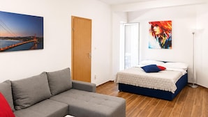 Un dormitorio moderno con un sofá gris, una cama con cabecera azul, una puerta de madera y un cuadro de un puente.
