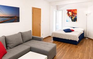 A modern bedroom with a grey sofa, a bed with a blue headboard, a wooden door, and a painting of a bridge. - 1 bedroom gorgeous apartment in Tribanj Sibuljina (Tribanj Sibuljina)