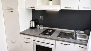 Una cocina moderna con gabinetes blancos, salpicadero negro, estufa a gas, un fregadero y un horno empotrado.