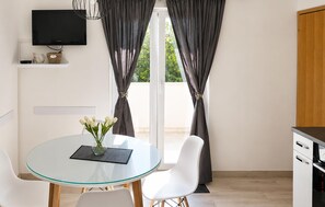 Ein modernes Zimmer mit Glastisch, weißen Stühlen, einem Fernseher und Blick aus dem Fenster.