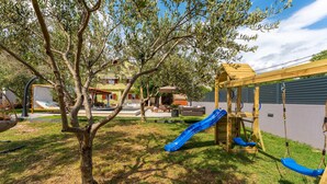 A playground with a slide and swings, surrounded by trees and a building.