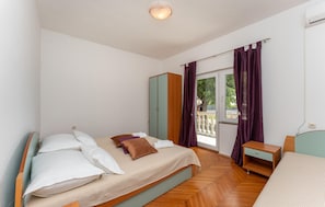 Un dormitorio con cama, armario, mesita de noche y ventana con cortinas.