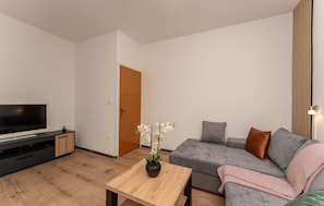 Una sala de estar moderna con un televisor de pantalla plana, un sofá gris, una mesa de centro de madera y una planta en maceta.