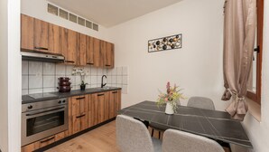 A compact kitchen with wooden cabinets, a black countertop, a dining table with chairs, and a decorative wall piece.