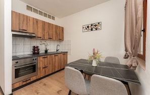Una cocina compacta con armarios de madera, una encimera negra, una mesa de comedor con sillas y un adorno en la pared.
