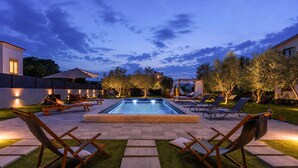 A swimming pool with lounge chairs and a pergola, surrounded by a well-lit patio area.