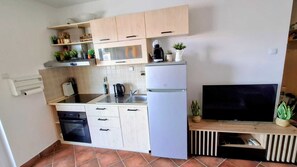 Eine kompakte Küche mit Mikrowelle, Herd, Kühlschrank und einem Fernseher auf einem Holzboden.