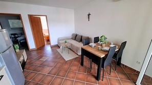 Ein Wohnzimmer mit einer Couch, einem Esstisch mit Stühlen, einem kleinen Tisch mit Pflanze und einem Kruzifix an der Wand.