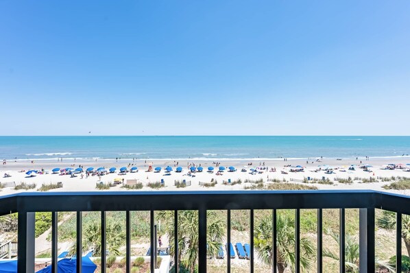 A beach view with umbrellas and lounge chairs, a clear sky, and a calm sea. - Nice 1BR Direct Oceanfront at Compass, Heated Pool (Myrtle Beach)