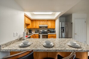 A kitchen with wooden cabinets, a stainless steel refrigerator, a microwave, and granite countertops. - Green Pines | Family Ski & Summer Retreat (Cottonwood Heights)