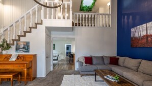 A spacious living area with a piano, a sofa, a coffee table, and a staircase leading to an upper level. - Green Pines | Bunk Room, Air Hockey & Canyons (Cottonwood Heights)