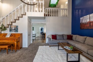 A spacious living area with a piano, a sofa, a coffee table, and a staircase leading to an upper level. - Green Pines | Family Ski & Summer Retreat (Cottonwood Heights)
